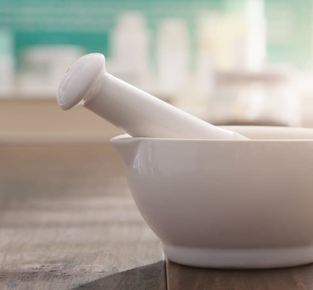 A white ceramic mortar and pestle on a wooden compounding bench at Triumph Pharmacy